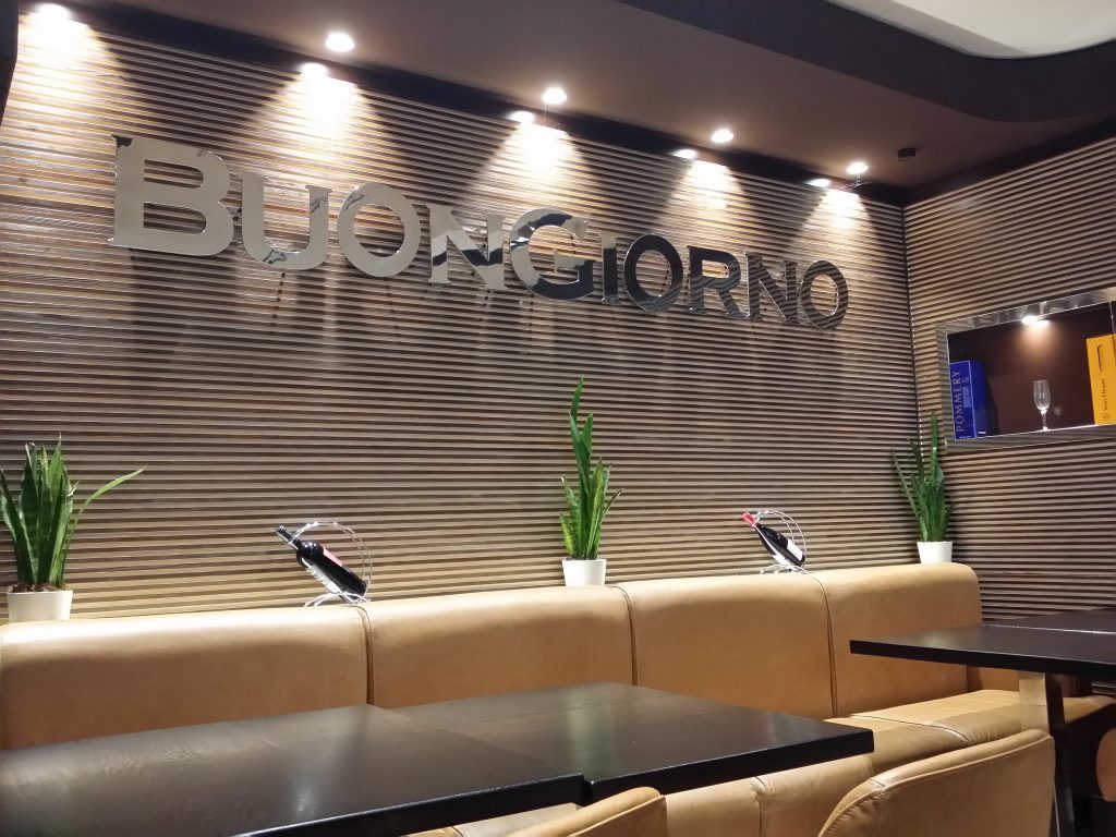 Wandverkleidung mit Schriftzug „Buon Giorno“ und Lederbank im Restaurant