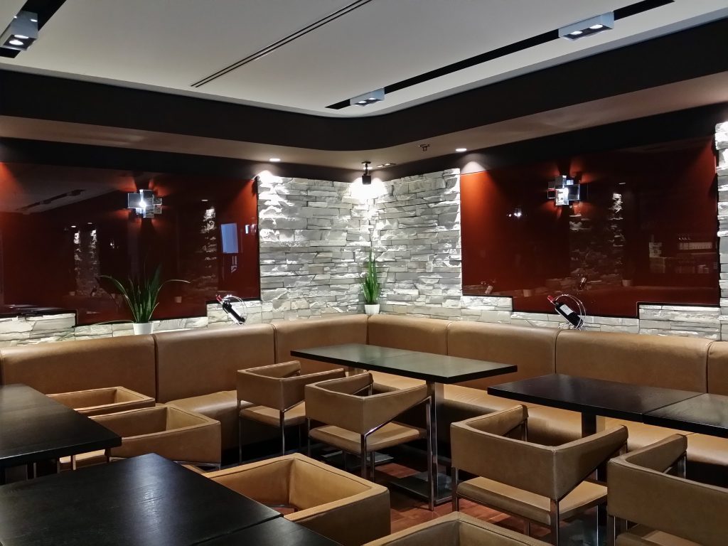 Lounge mit Ledersesseln, Natursteinwand und roter Glaswand in einem Restaurant